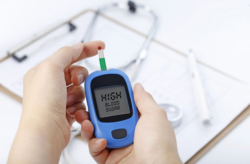 A hand-holding Glucometer with high blood sugar was written on the result. High blood sugar on diabetic person may lead to Diabetic Retinopathy.