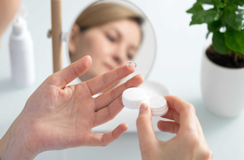 A woman holding a contact lens on her finger, looking in the mirror to put them in