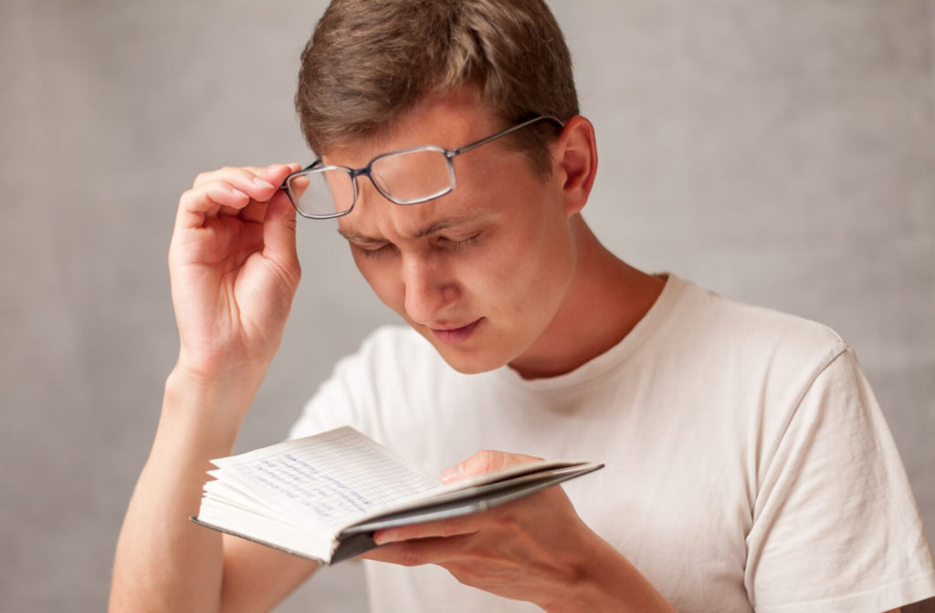 A young man holding a notebook close to his face and squinting to see what is written on the pages.