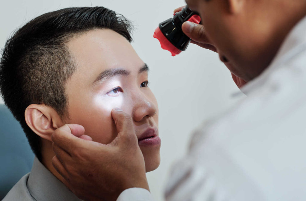 An optometrist shining a small flashlight into a man's right eye