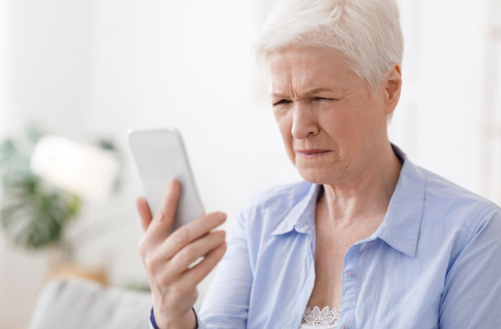 A senior woman squinting her eyes to see more clearly while holding a phone in her right hand