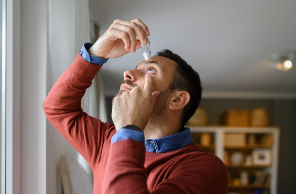 A man is placing lubricating eye drops in his eye to aid with dry eye symptoms.