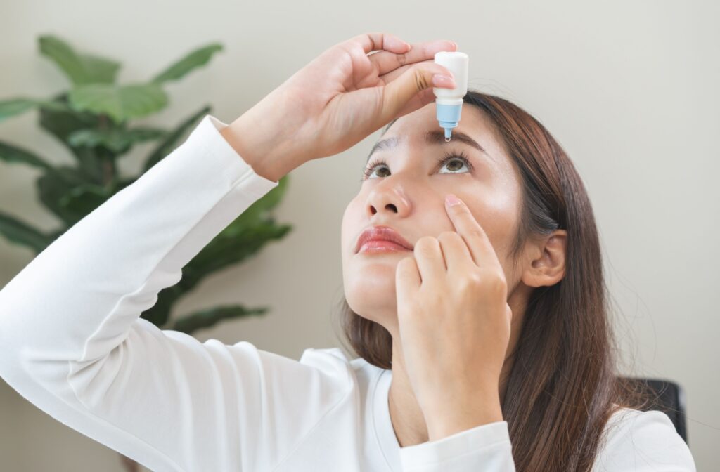 A young adult carefully applying eye drops to their left eye to reduce their dry eye symptoms.