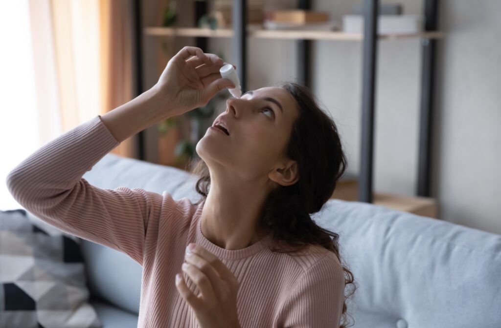 An adult tilts their head back while sitting on a couch to apply eye drops to relieve dry eye symptoms