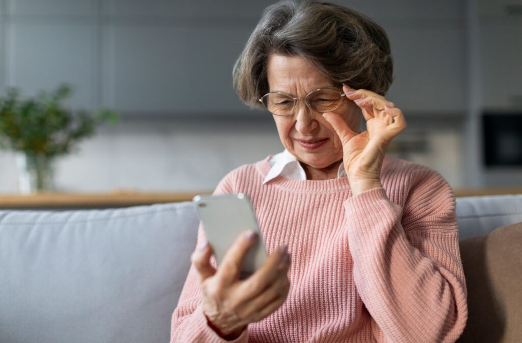 An older person squints as they try to read their smartphone on the couch.