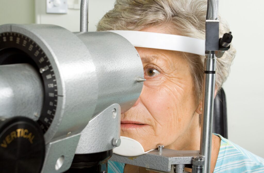 An older person undergoes an eye exam, sitting in front of a diagnostic machine while looking through a vision testing device.
